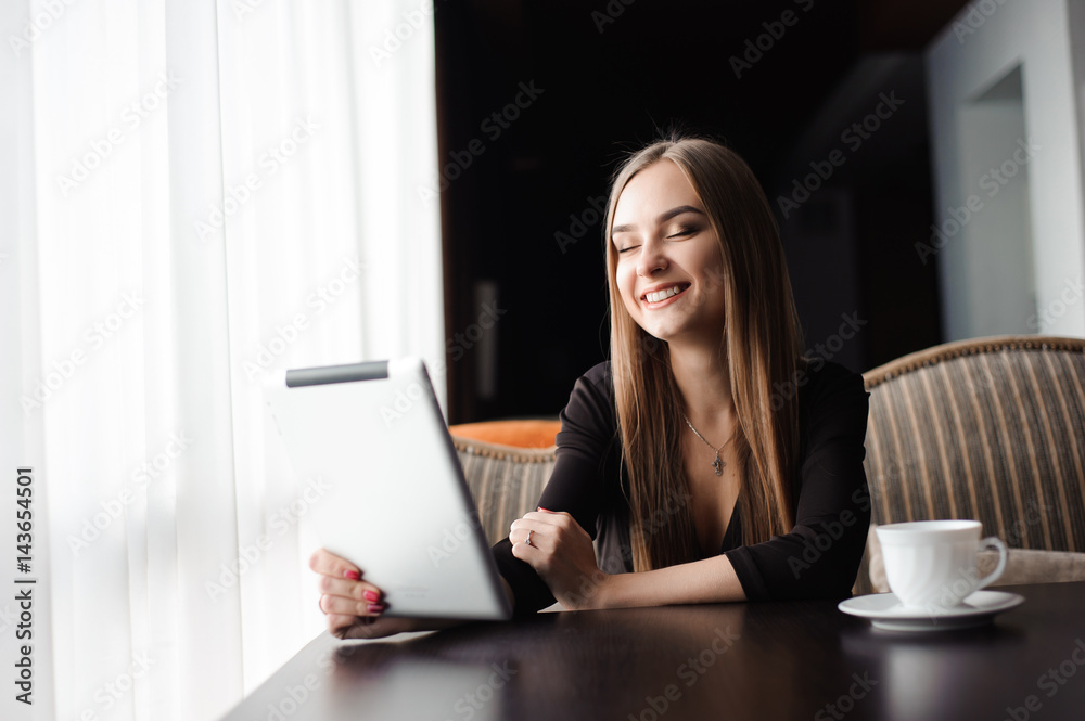 Happy young woman drinking coffee / tea and using tablet computer in a coffee shop Happy young woman drinking coffee / tea and using tablet computer in a coffee shop