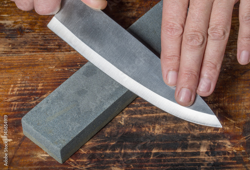 Knife sharpening. Hands holding knife and whetstone on  the old wooden cutting board. photo