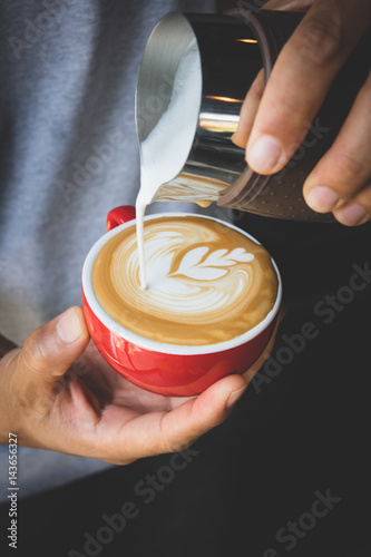 Vertical image of pouring milk to espresso coffee make latte art on red cup coffee