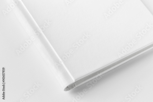 Mockup of closed blank square book at white textured paper background. Angle view