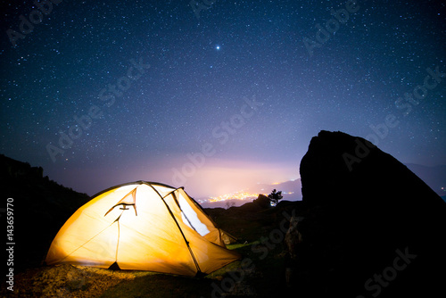 Glowing tent in the mountains under a starry sky