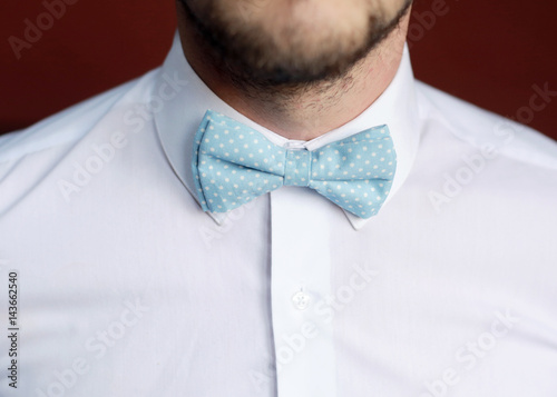 Fashion photo of a man with beard correcting his bowtie 