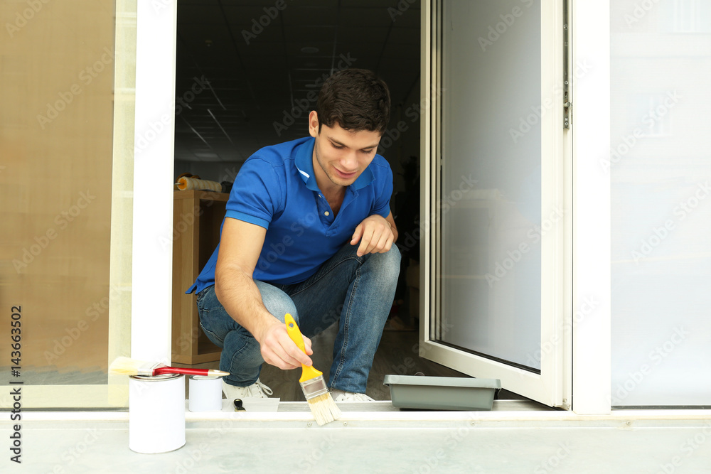 Young man painting window at home Young man painting window at home