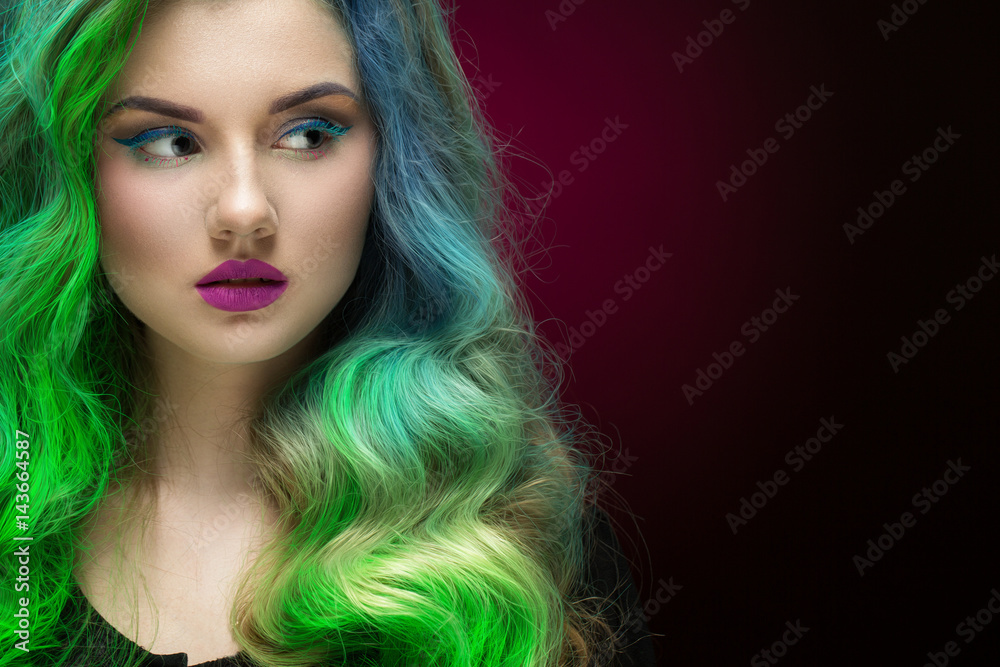 Mystic look. Closeup portrait of a beautiful green haired woman wearing colorful makeup looking at the copyspace on the side on black and red gradient background