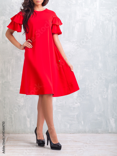 Attractive slender girl blonde with curly hair in bright red fashionable dress posing in studio.