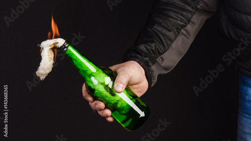 Glass bottle, the so-called Molotov cocktail in the hand of the activist. Isolated on a black background. photo