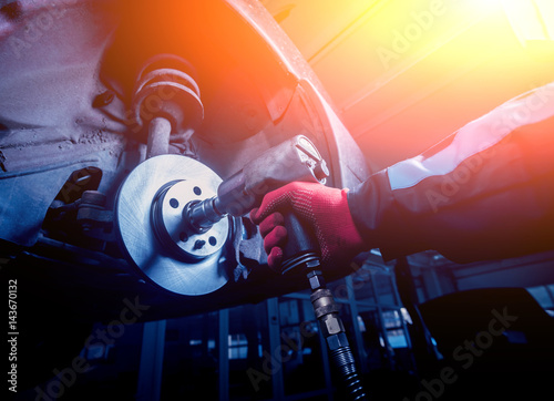 Professional car mechanic working with pneumatic wrench in auto repair service. photo