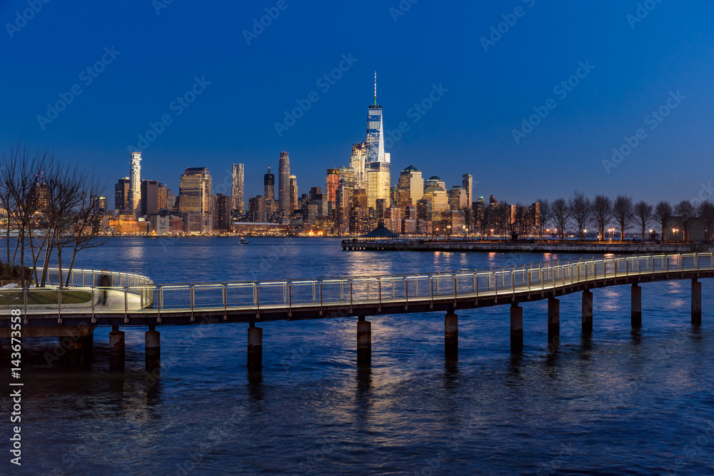 New York City Financial District skyscrapers at sunset and Hudson River from Hoboken promenade. Lower Manhattan skyline and pedestrian bridge from New Jersey