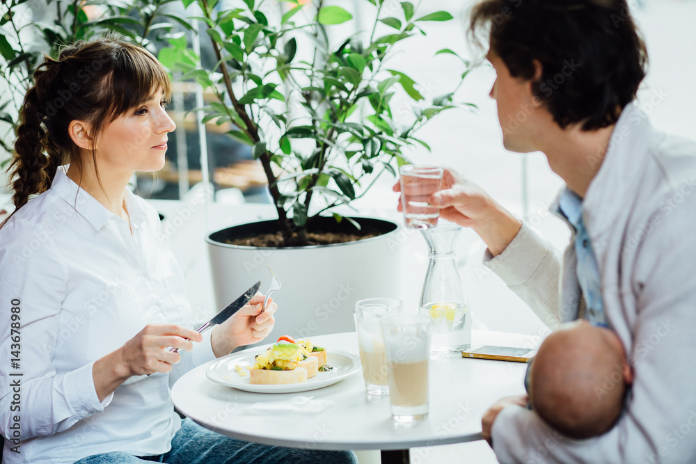 Happy family of three spending time together: they are having breakfast in cafe or restaurant interior. Parenthood, love and happiness concept. Happy family of three spending time together: they are having breakfast in cafe or restaurant interior. Parenthood, love and happiness concept.