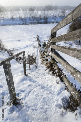 beautiful winter rural landscape with river, steep bank, trees, wooden stairs and snow