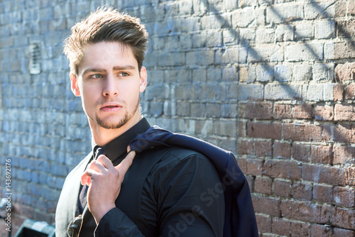 Handsome man posing in the street holding a jacket over his shoulder. photo