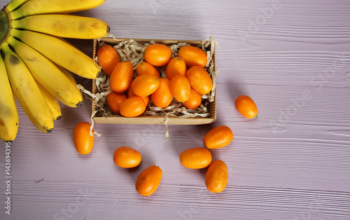 kumquat and bananas on the violet wooden background