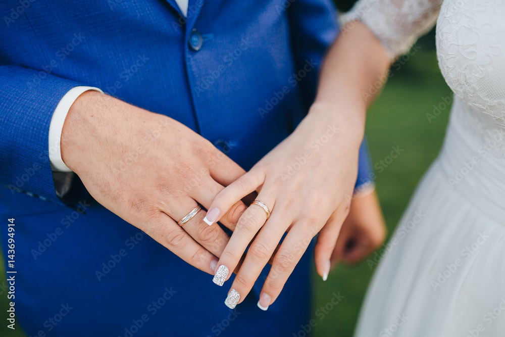 Groom in a blue suit and bride in a white dress holding hands on the fingers of the bride and groom wedding rings Groom in a blue suit and bride in a white dress holding hands on the fingers of the bride and groom wedding rings