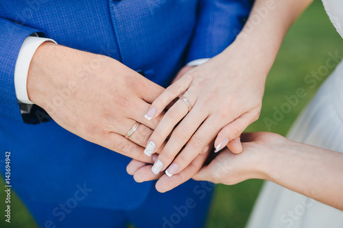 Groom in a blue suit and bride in a white dress holding hands on the fingers of the bride and groom wedding rings