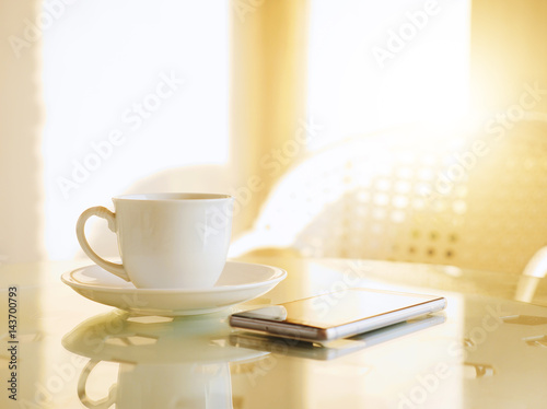 Coffee cup on table and smartphone with sunlight in morning