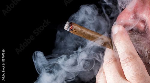 Foto A man smokes a cigar against black background