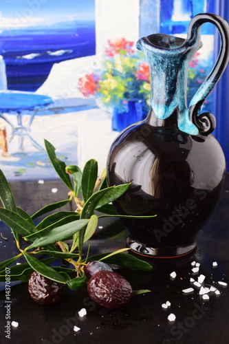 Traditional Greek ceramic olive oil jar with lemon, sea salt, olives, brunch of olive tree on a dark back ground. photo