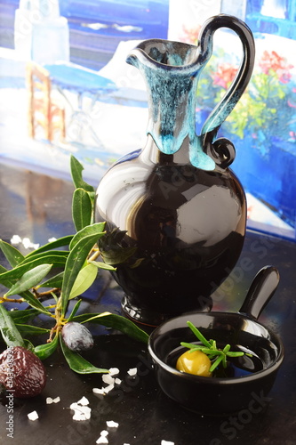 Traditional Greek ceramic olive oil jar with lemon, sea salt, olives, brunch of olive tree on a dark back ground. photo