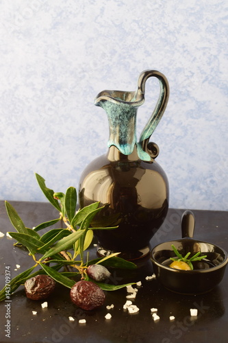 Traditional Greek ceramic olive oil jar with lemon, sea salt, olives, brunch of olive tree on a dark back ground. photo