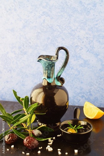 Traditional Greek ceramic olive oil jar with lemon, sea salt, olives, brunch of olive tree on a dark back ground. photo
