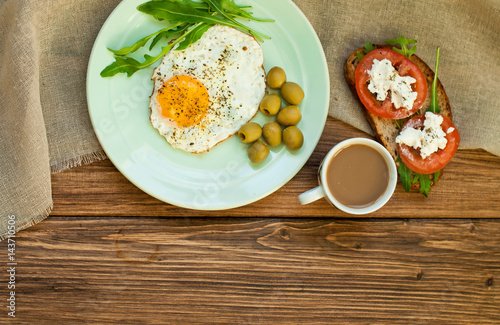 Fried eggs, a sandwich with vegetables and feta cheese and cappuccino coffee for breakfast. Tomatoes and bread on a wooden table
