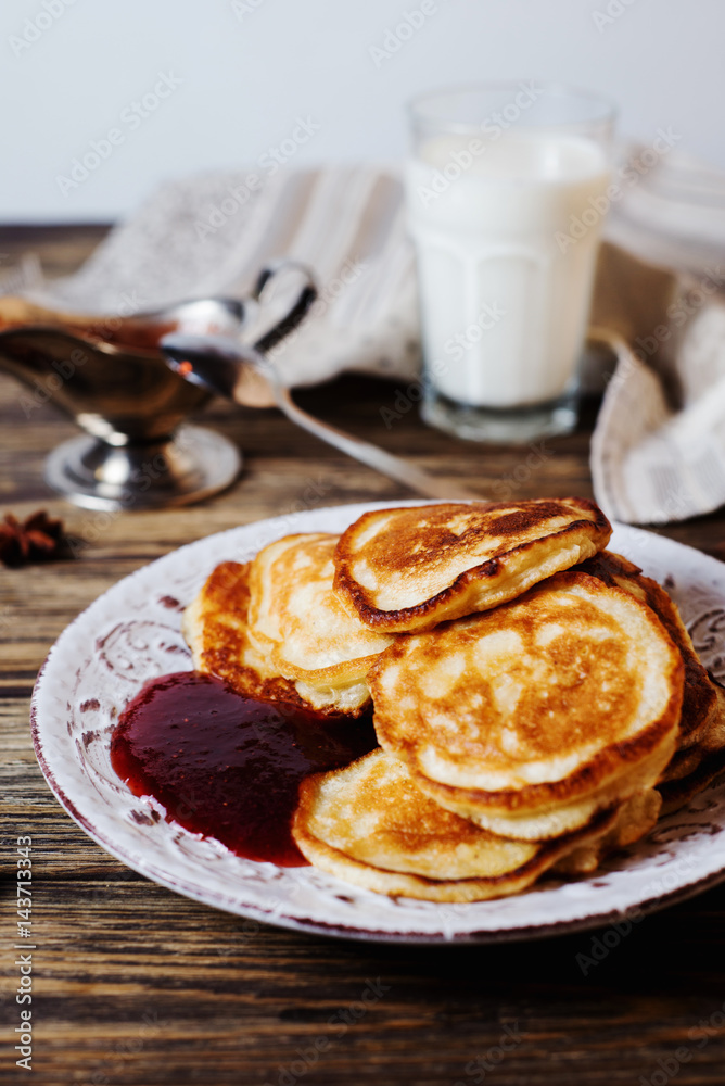 Hearty and tasty breakfast or lunch, fried pancakes with strawberry jam, milk and black tea on a dark wooden background Hearty and tasty breakfast or lunch, fried pancakes with strawberry jam, milk and black tea on a dark wooden background
