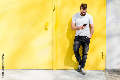 Colorful portrait of a handsome man dressed in white t-shirt and jeans with phone on the yellow background