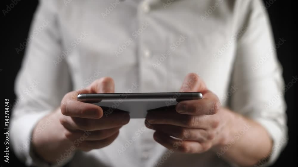 Concept, digital online life and social networks. A businessman in a shirt uses his smartphone to view his accounts. Expressive shot, a man in a dark room, holding a stylish phone Concept, digital online life and social networks. A businessman in a shirt uses his smartphone to view his accounts. Expressive shot, a man in a dark room, holding a stylish phone