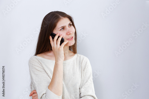 Portrait of young woman talking on the phone. Human reaction, expression. Grey background.