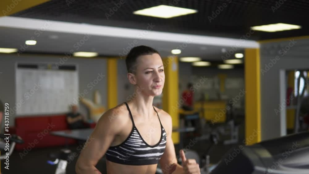 The fitness coach shows the correct position of the hands and deep breathing during running. A woman is actively engaged in sports on a treadmill in the fitness club.
