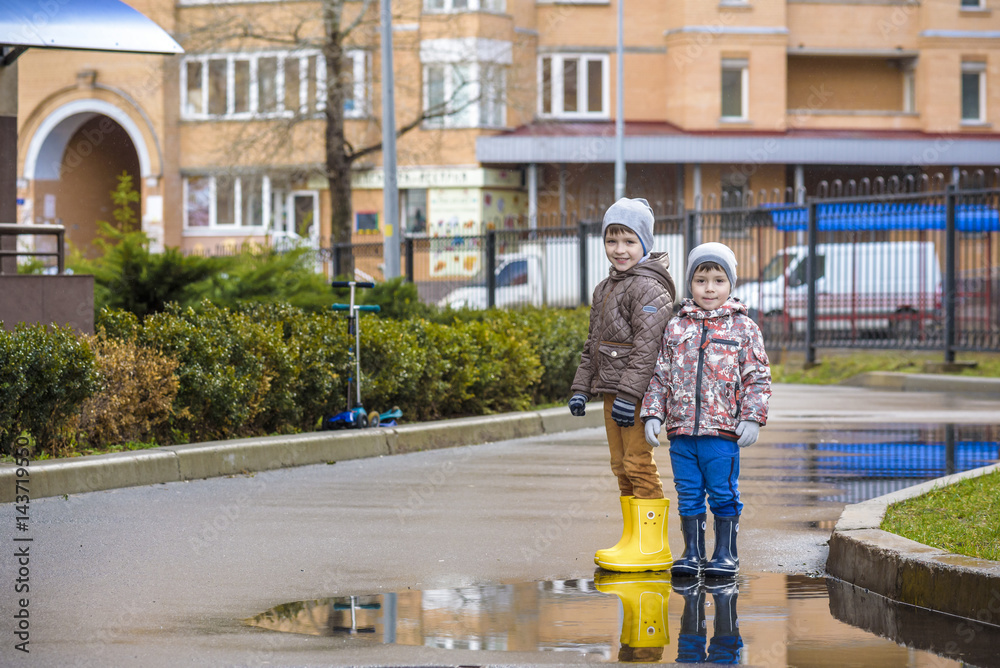 Two little boys, squat on a puddle, with little umbrellas
