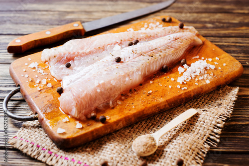 Fresh raw fish, fillet of hake with spices, black pepper and salt on a wooden board, background  photo