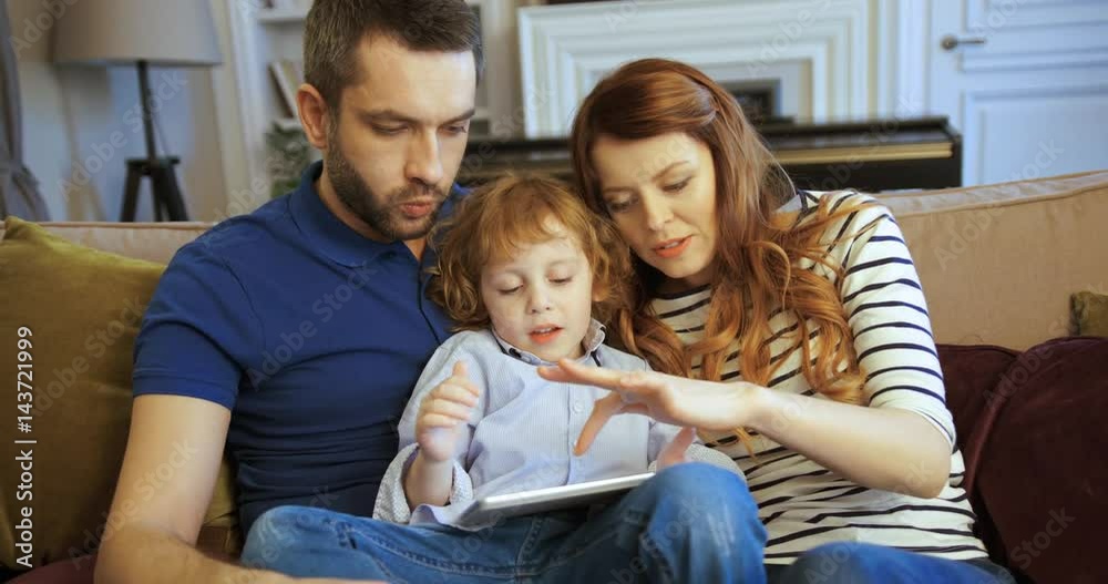 Mother, father and son using tablet, playing games, watching videos and having fun. Family spending time together at home. Happy family Mother, father and son using tablet, playing games, watching videos and having fun. Family spending time together at home. Happy family