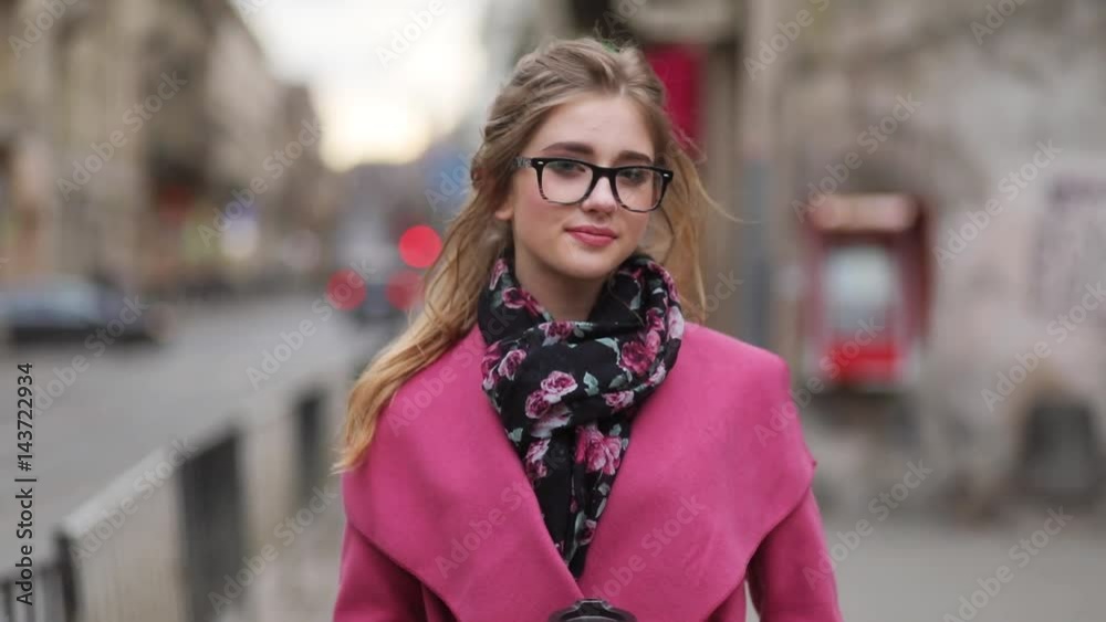 Lovely young girl in an elegant look walking down the crowded city street, with a cup of coffee and looking direct in the camera. Busy lifestyle. Business-lady. Urban background. Lovely young girl in an elegant look walking down the crowded city street, with a cup of coffee and looking direct in the camera. Busy lifestyle. Business-lady. Urban background.