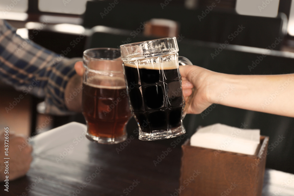 People cheering beer glasses over table in pub, closeup People cheering beer glasses over table in pub, closeup