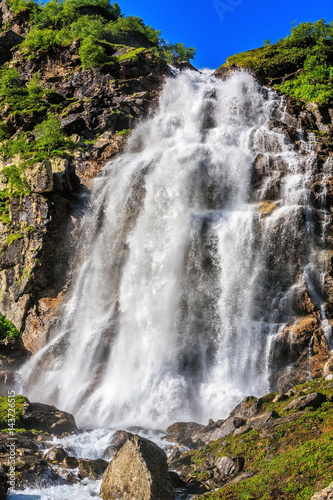 Beautiful scenic landscape of Caucasus mountain waterfall on Imeretinka river at summer in sunlight with splashes and blue sky. Vertical scenery