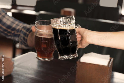People cheering beer glasses over table in pub, closeup