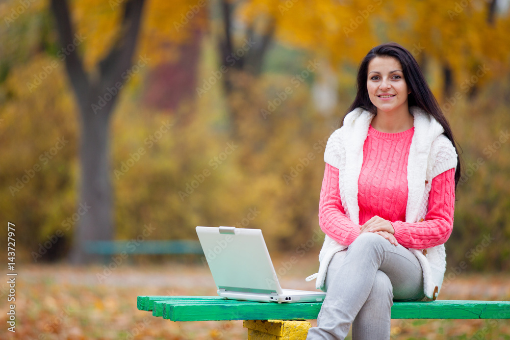 photo of beautiful young woman sitting on the bench with laptop on the wonderful autumn trees background photo of beautiful young woman sitting on the bench with laptop on the wonderful autumn trees background