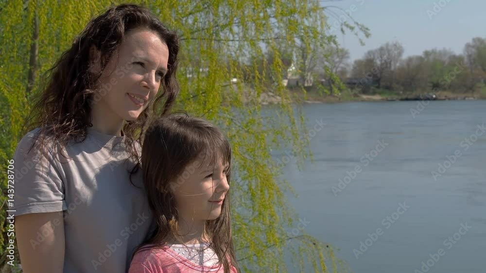 Mom and daughter on the river bank. Woman with child on a sunny day by the water. Slow motion. Mom and daughter on the river bank. Woman with child on a sunny day by the water. Slow motion.