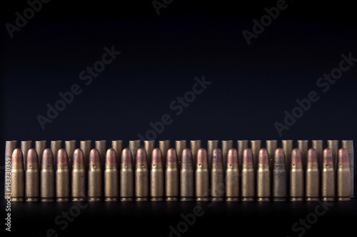 A lot of old gun bullets standing precisely in a row on the dark background