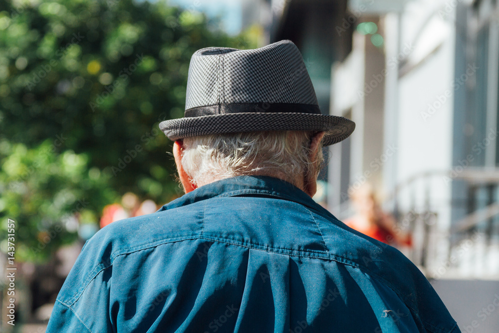 Old man with hat seen from behind walking down the street