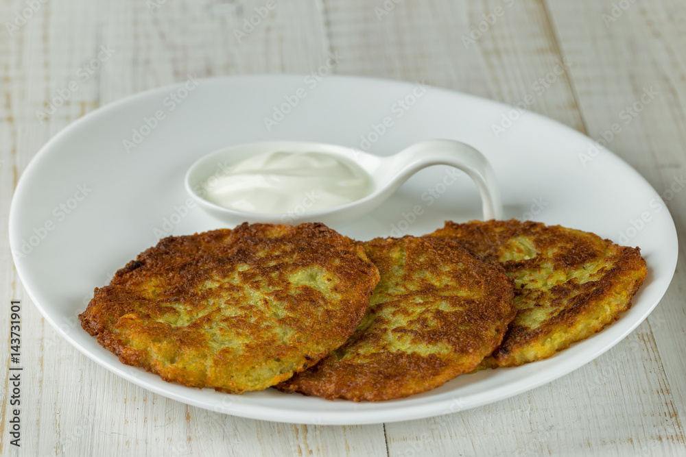 Potato pancakes on a white plate with sour cream Potato pancakes on a white plate with sour cream