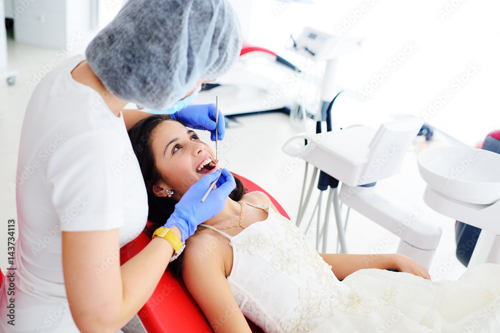 Dentist girl treats teeth to baby girl in smart dress in red dental chair Dentist girl treats teeth to baby girl in smart dress in red dental chair