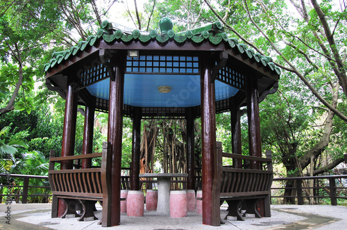  Chinese pavilion with green roof and brown columns, stone table and stools under the pavilion.