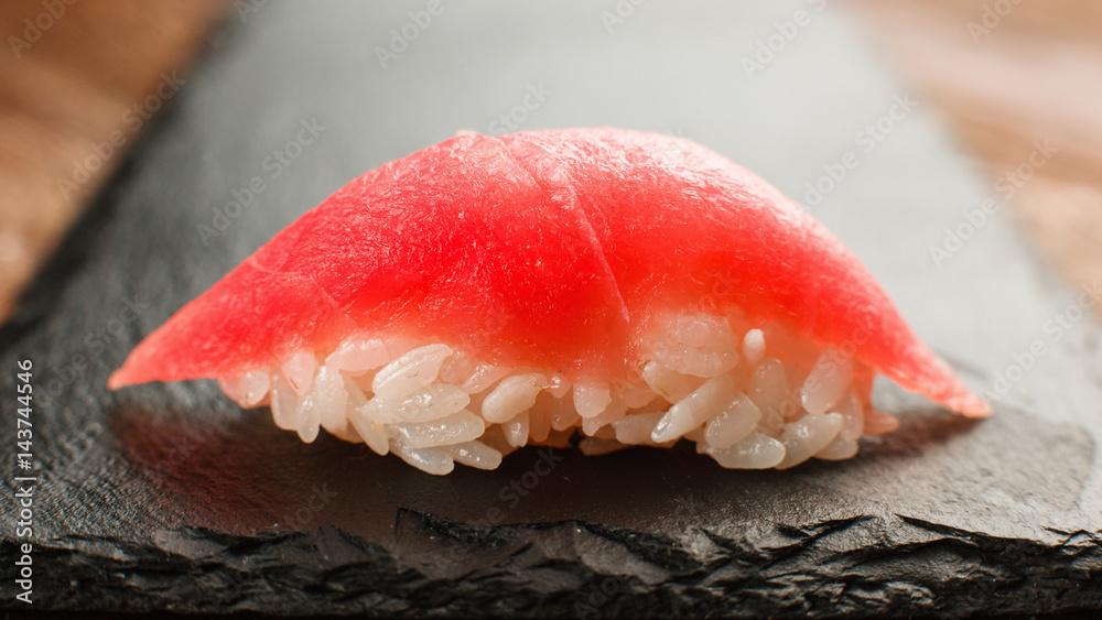 Japanese traditional and healthy seafood. Tasty and fresh one nigiri sushi with appetizing tuna, served on black slate, close up view. Japanese traditional and healthy seafood. Tasty and fresh one nigiri sushi with appetizing tuna, served on black slate, close up view.