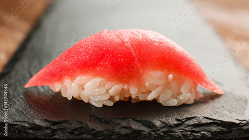 Japanese traditional and healthy seafood. Tasty and fresh one nigiri sushi with appetizing tuna, served on black slate, close up view.