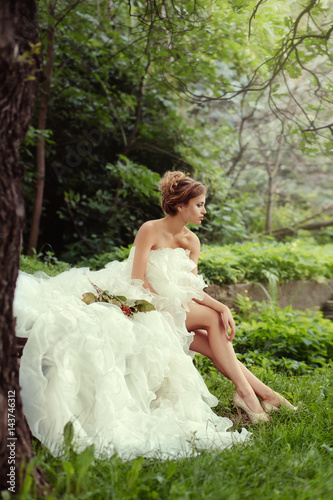 Portrait of a beautiful bride woman sits in a profile and looks into the distance in nature.
