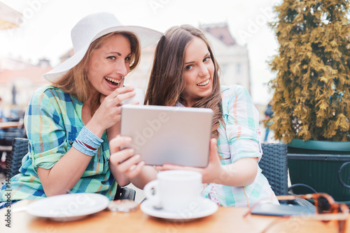 Two beautiful women sitting in the cafe after shopping, drinking coffee and having fun with tablet. Consumerism, lifestyle concept