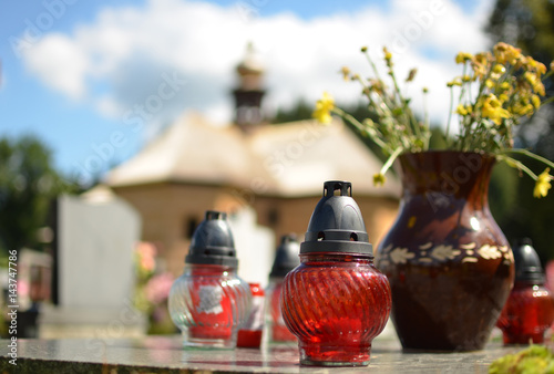 Candles, vase on the grave and old wooden church in the background