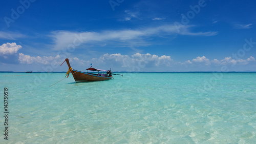 Wooden boat on a turquise blue sea with white clouds on a horizon © Sead